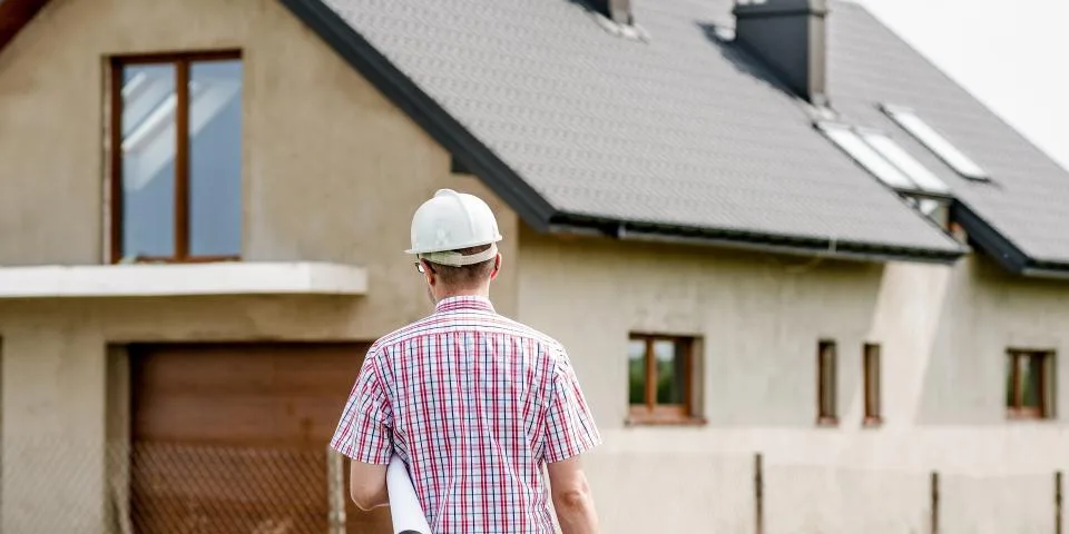 A site manager carrying plans towards a newly built house