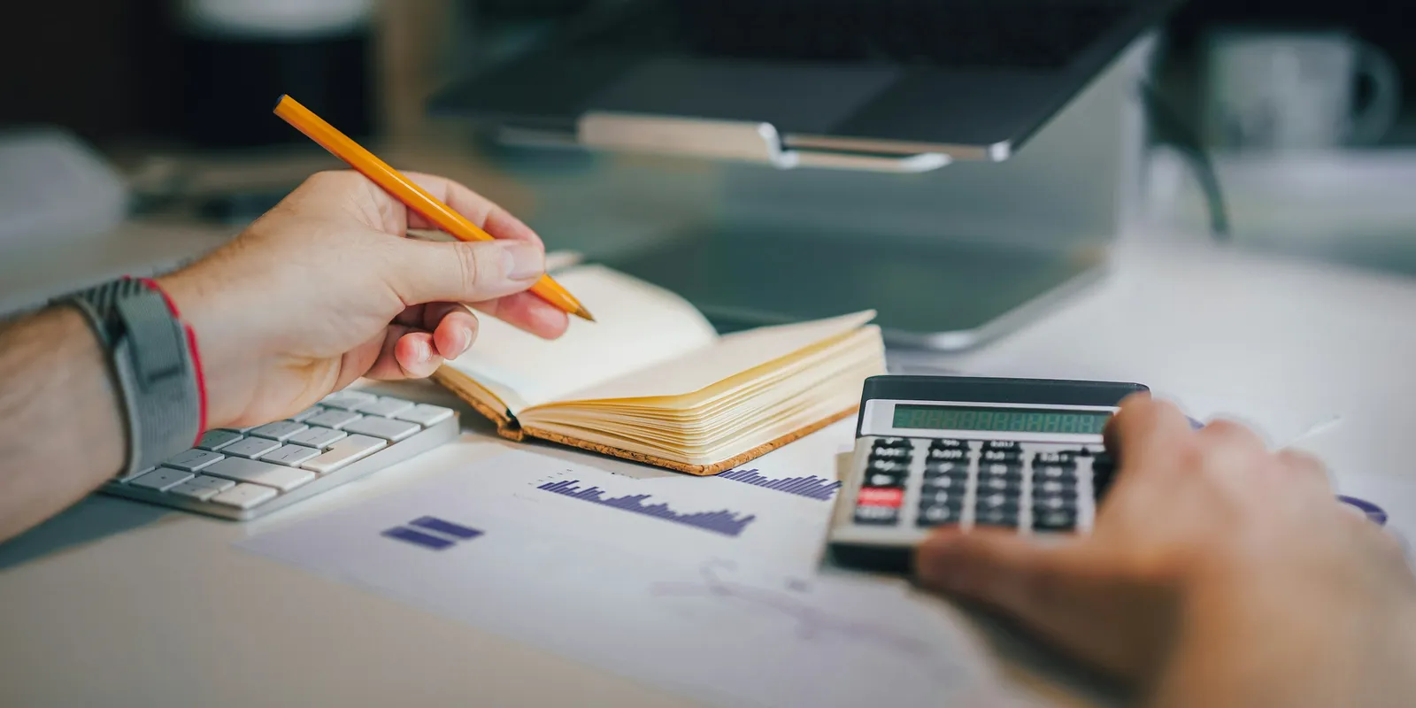 Hands working through figures with a calculator, notebook and printed charts